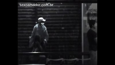 Mulher faz sexo oral no parceiro, em parada de &ocirc;nibus na rua